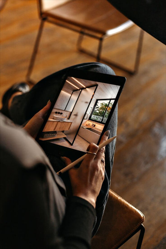 Person holding a tablet with interior design images on a wooden floor.