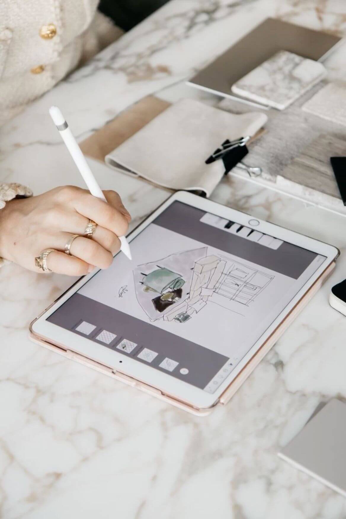 Person using a stylus on a tablet with architectural drawing on a marble surface