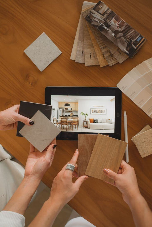 Two people holding color swatches over a tablet displaying a room design on a wooden table.